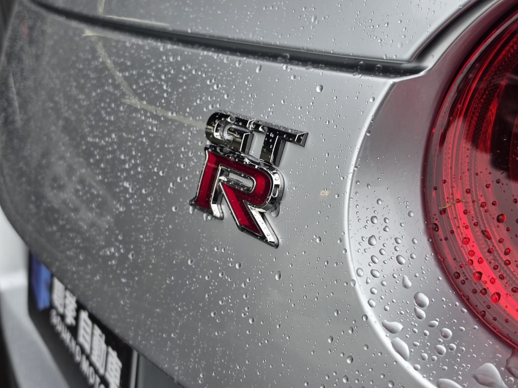 リアクオーターの GT-R エンブレム。雨粒が銀の塗装に張り付く